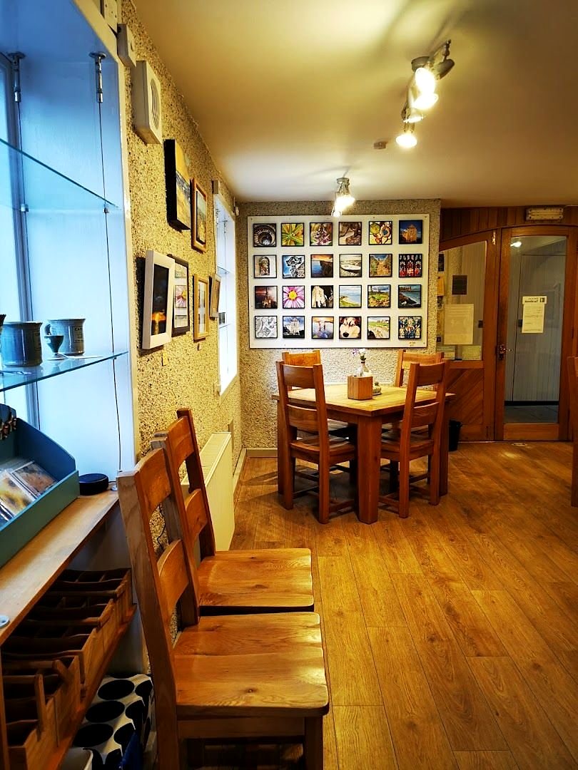 Inside the café: wooden chairs and tables on a wooden floor, and a pale wall hung with a grid of small square pictures